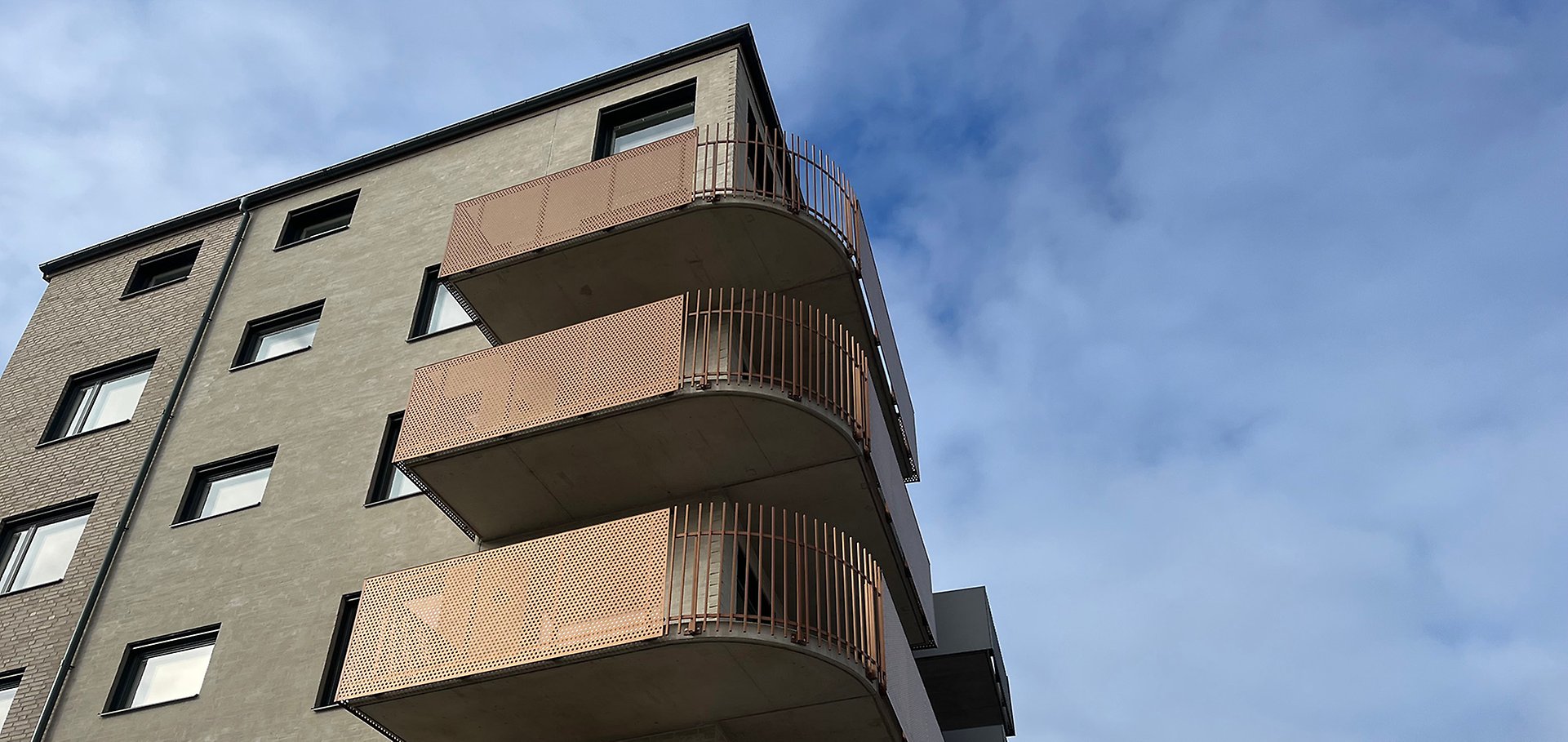 Fasaden på kvarter 8. Husgaveln är rundad i grått tegel och balkongerna böjer sig runt husknuten.