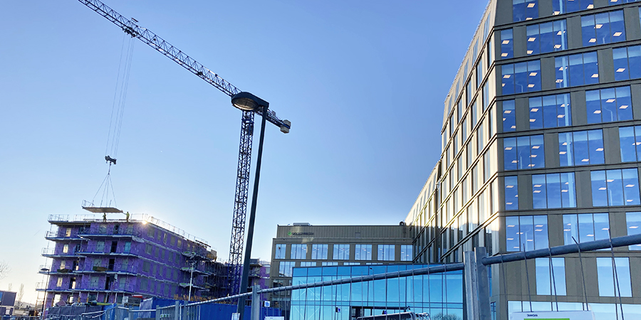 Delar av en stor kontorsbyggnad med guldig fasad och stora fönster syns, liksom en byggkran och pågående uppbyggnad av ett bostadsrätts-hus.
